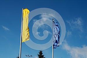 Two flags, yellow and blue, flutter in the wind across the sky on a sunny day