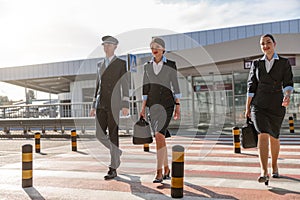 Two flight attendants with bags and their colleague crossing the road