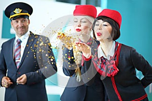 Two flight attendants in red hats blow away gold photo