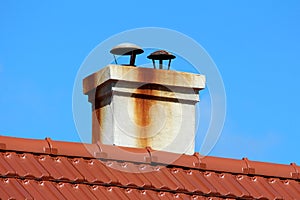 Two flue metal pipes chimney with rusted protection caps on top encased in concrete with dirty rust and smoke chimney stains