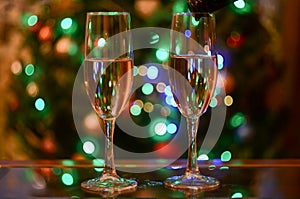 Two flute glasses with champagne against Christmas tree bokeh background