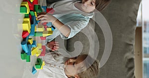 Two focused cute sibling kids playing building blocks at home