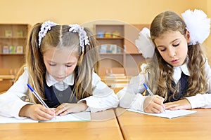 Two focused girls in uniform sit at wooden school photo