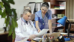 Two focused physicians working together with case histories on laptop in modern clinic office