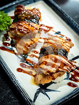 Two foie gras sushi with sauce served on white plate on dark table, Japanese food style.