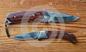 two folding knives with wooden handles in the open state on a brown wooden background