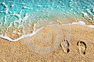 Two footprints on yellow sand, blue sea wave, white foam top view close up, turquoise ocean water, summer vacations concept