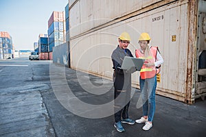 Two foreman man & woman worker working checking at Container cargo harbor holding laptop computer and using walkie-talkie to