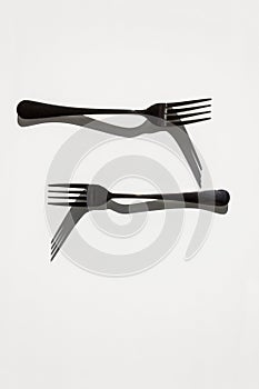 Two forks with sharp shadows of sun on a white background. Menu design concept.