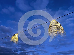 two frayed straw outdoor lamps lit at blue hour with a sky with clouds in a chill out atmosphere, summer nights at the beach at