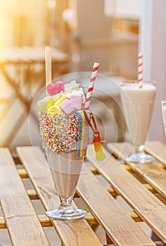 Two freak shakes with marshmallow, meringue and marmalade on a wooden table in a cafe