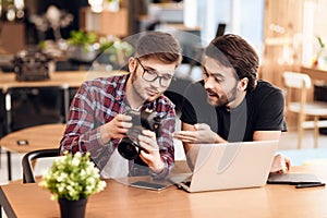 Two freelancer men looking at photos at laptop at desk.