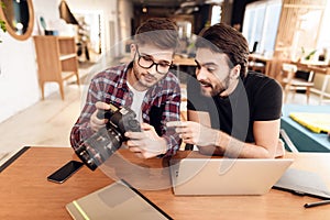 Two freelancer men looking at photos at laptop at desk.