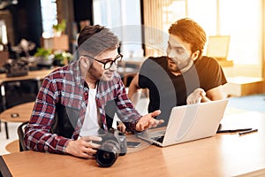 Two freelancer men looking at photos at laptop at desk.