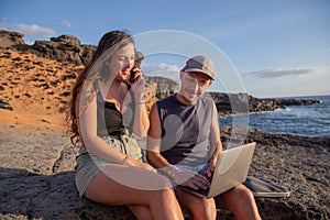 Two freelancers work at the beach, girl makes a phone call, boy uses laptop