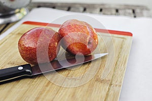 Pair of Amigo Pluots on a Wood Chopping Board with a Knife photo