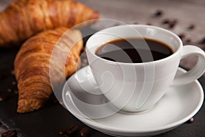 Two fresh croissants and cup of coffee on dark stone table