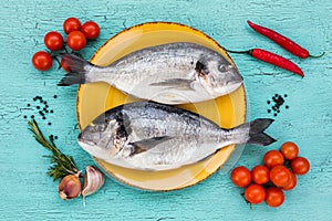 Two fresh dorado fish on yellow plate and vegetables on blue table