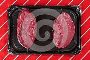 Two fresh fillet steaks on a plastic tray on a red and white butcher apron. Meat and retail industry concept. Premium cut of beef