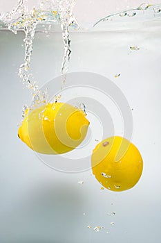 Two Fresh lemons in water splash on white