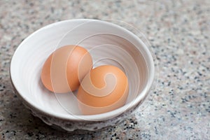 Two fresh light brown eggs in a cup on a granite table