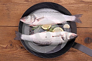 Two fresh moronidae fish on frying pan with ingredient