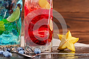 Two fresh multi-colored cocktails with mint, lime, carambola, ice and berries on a wooden background. Refreshing summer beverages.