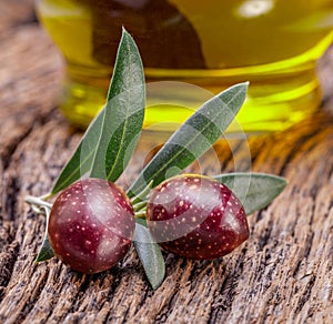 Two fresh olives on olive twig on old wooden background and glass olive bottle at the background