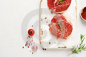 Two fresh Parisienne raw steak on white parchment paper with salt, pepper and rosmary in a rustic style on old wooden background.