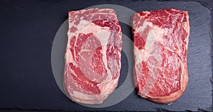 Two fresh raw marble meat, black Angus ribeye steak on a dark stone background.
