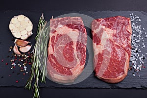 Two fresh raw marble meat, black Angus ribeye steak with spices on a dark stone background