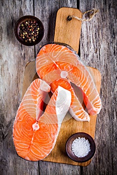 Two fresh raw salmon steaks on a cutting board with salt and pepper