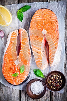 Two fresh raw salmon steaks on paper with salt, peppers, lemon, and basil
