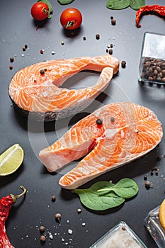 Two fresh raw salmon steaks with peppers, lemon on black background