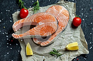 Two fresh raw salmon steaks with salt, peppers, lemon, tomatoes and rosemary on the rustic paper