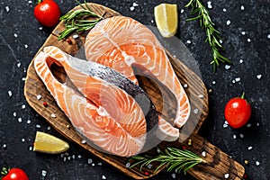 Two fresh raw salmon steaks with salt, peppers, lemon, tomatoes and rosemary on the rustic table