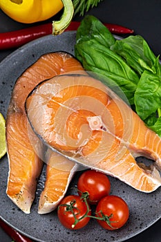 Two fresh raw salmon steaks with vegetables and spices: rosemary, tomatoes, peppers, basil, lemon and olive oil