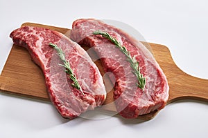 Two fresh raw striploin steak on wooden board on white background with rosmary side view