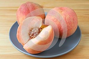 Two Fresh Ripe Peach Whole Fruits and One Cut Peach on a Blue Plate Served on Wooden Table