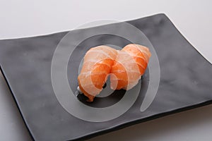 Two fresh salmon sushi on a black dish