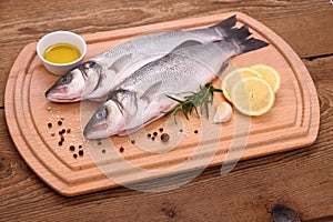 Two fresh sea bass fish on cutting board with ingr