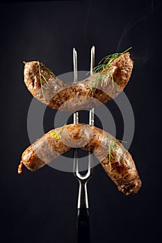 Two fried beef sausages on a fork. The concept of a delicious lunch for a hotel on a black background