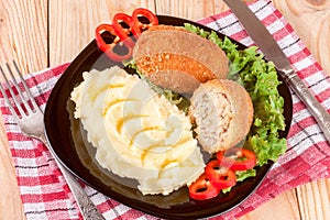 Two fried breaded cutlet with mashed potatoes and lettuce on a black plate wooden background