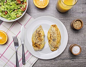 Two fried chicken breasts with curry, fresh orange juice, fresh salad nutrition athletes wooden rustic background top view