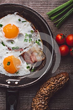 Two fried eggs with bacon and onion, tomato and bread on the side