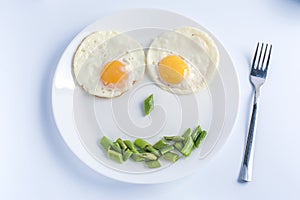 Two fried eggs with green beans on white plate, fork on light background.