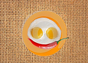 Two fried eggs and red hot chilly pepper on orange plate, knife