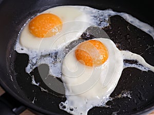 Two fried eggs seasoned with sea salt in a frying pan