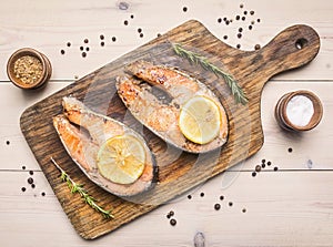 Two fried fresh salmon steak with unground pepper, spices , lemon on a cutting board top view