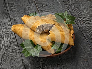 Two fried pies with herbs in a clay bowl on a wooden table